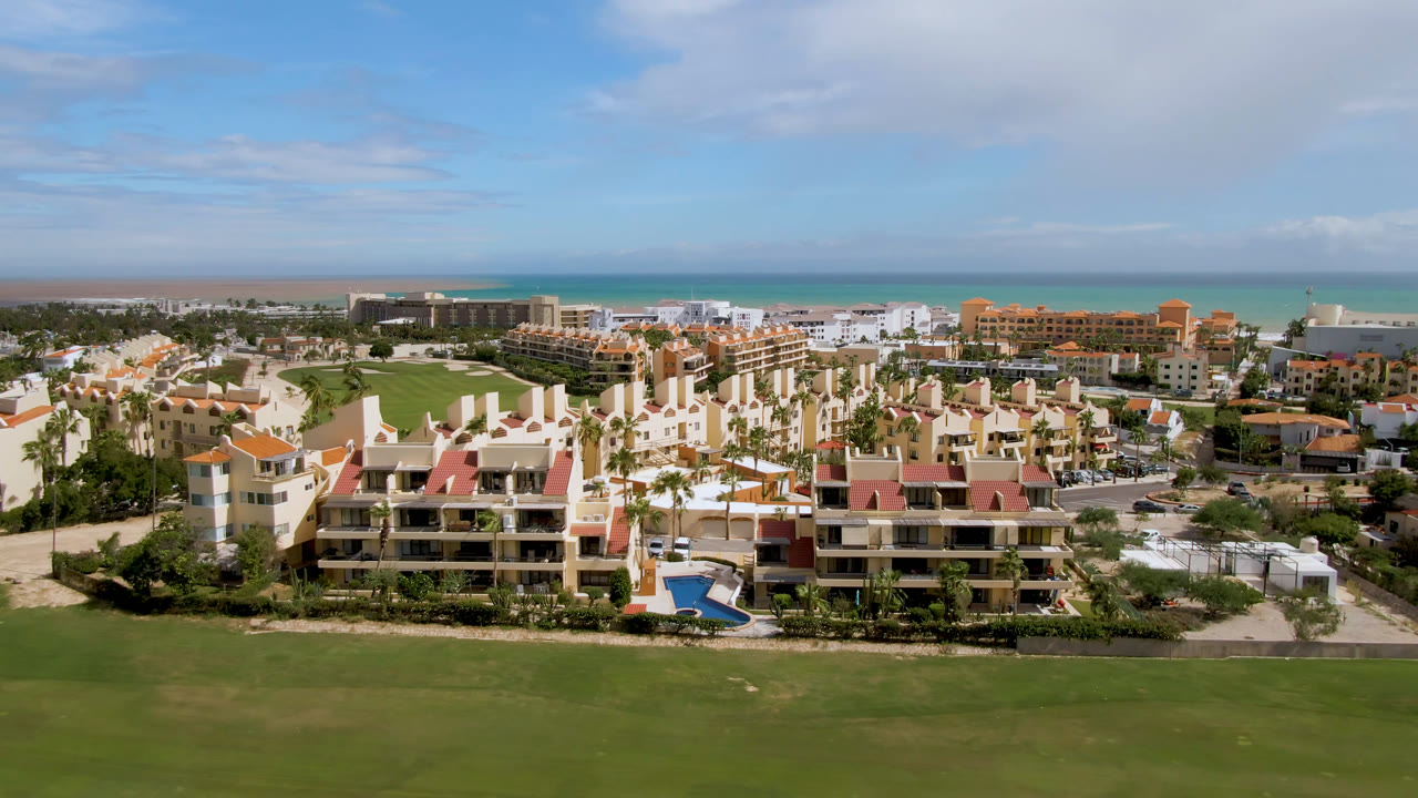 Wide aerial of golf course foreground with resort and ocean behind