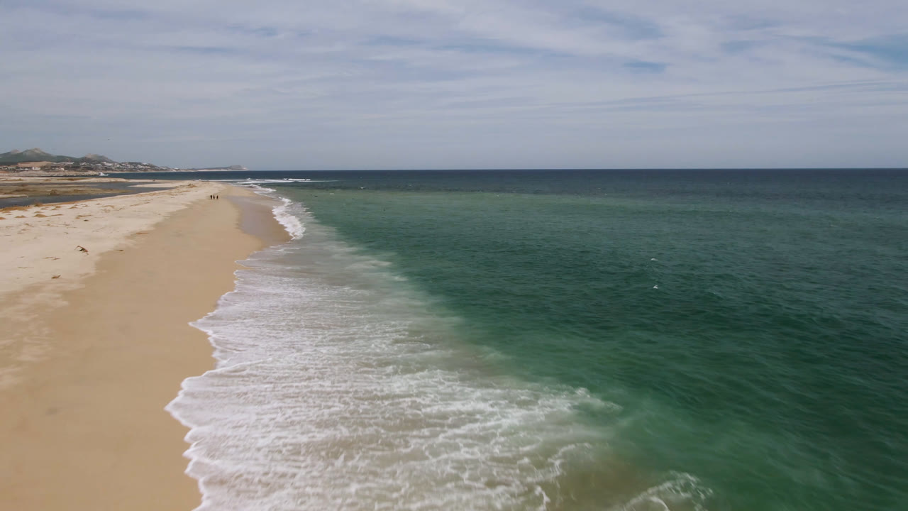 Aerial coastline with curved beach, surf, and open ocean.