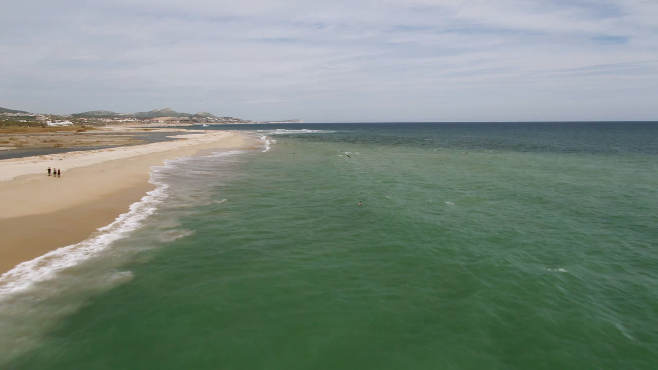 Elevated view of green ocean water meeting a sandy San Jose del Cabo beach, with distant coastline and no visible people.