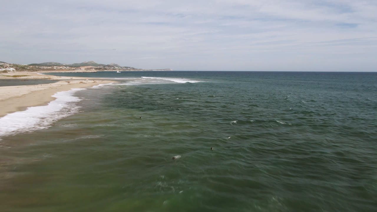 Wide aerial shoreline view with white surf, green water, and a distant coast.