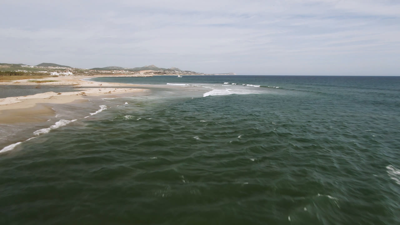 Wide aerial beach and ocean frame with white surf near the shoreline.