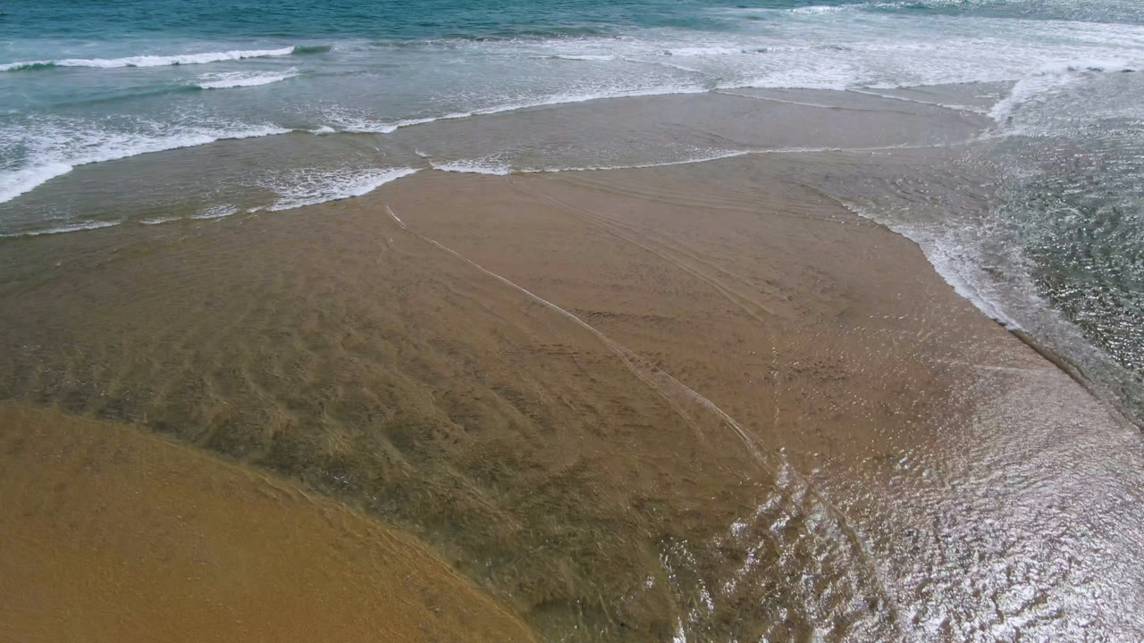 Aerial shoreline frame from San Jose del Cabo with a broad sheet of wet sand, green-blue water near the top, and no visible people.