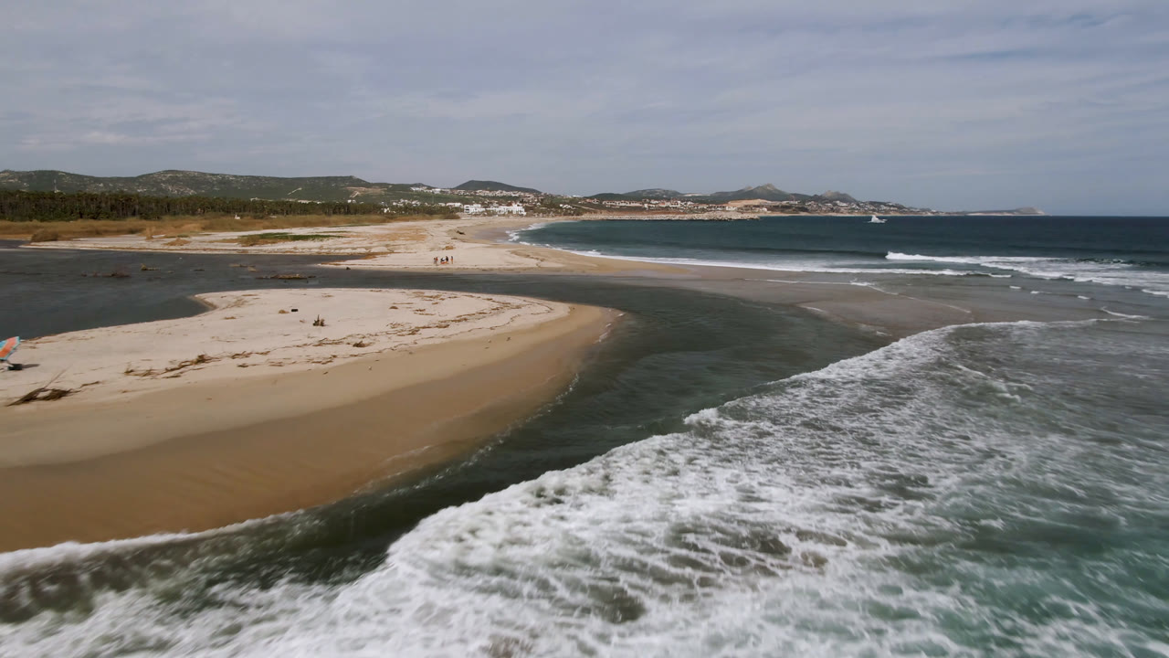 Aerial view of a sandy beach, tidal channel, and ocean surf.