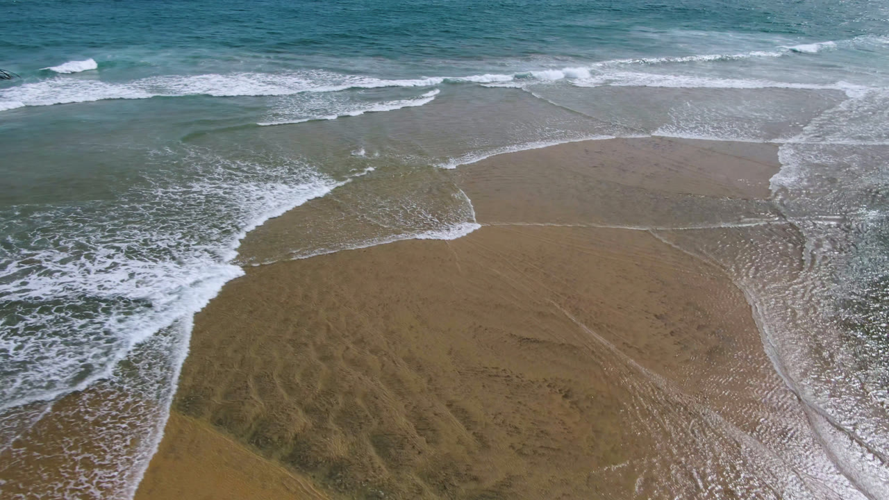 Overhead surf foam crossing wet sand and shallow ocean water.
