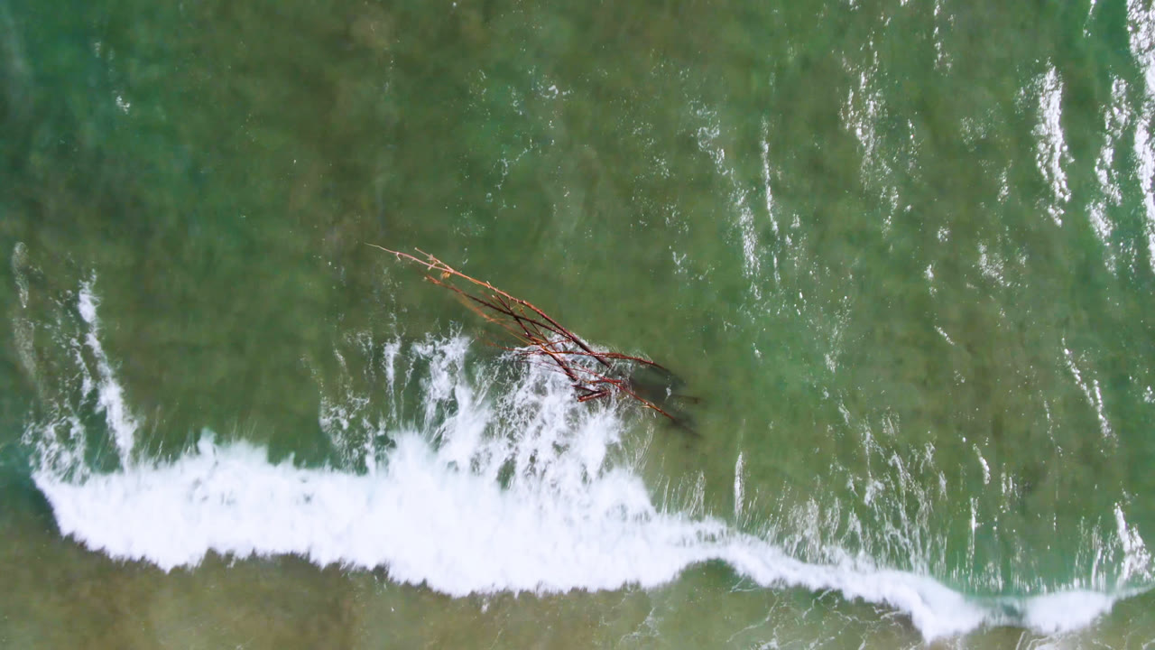Aerial view of surf foam and a wooden structure in green coastal water