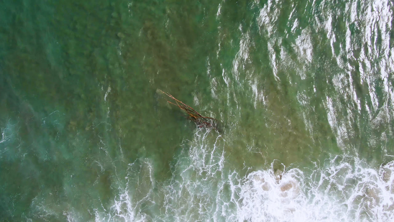 Overhead view of green-blue water and white surf in San Jose del Cabo with a small dark brown object near the upper left area and no visible people.