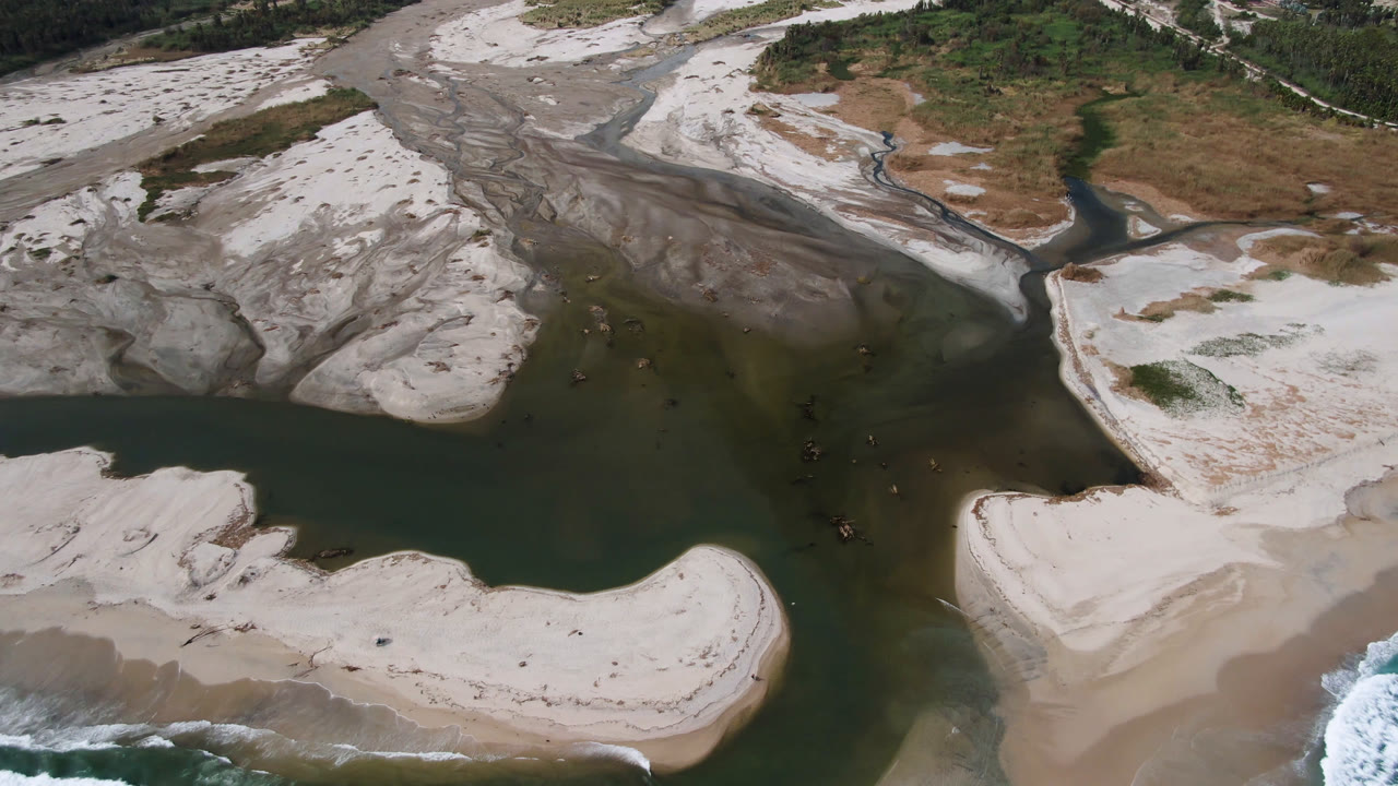 Overhead aerial frame in San Jose del Cabo showing dark river water between pale sand banks, gray erosion channels, sparse vegetation at the top, and no visible people.
