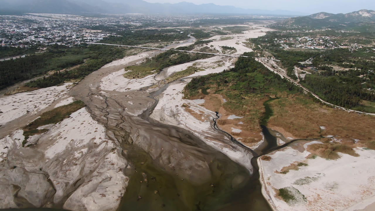 Drone view of a dry wash with branching water channels and green brush.