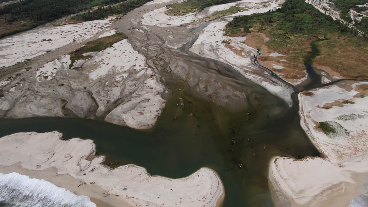 Aerial view over San Jose del Cabo river channels, gray eroded sand flats, green-brown water, and scrub vegetation, no visible people.