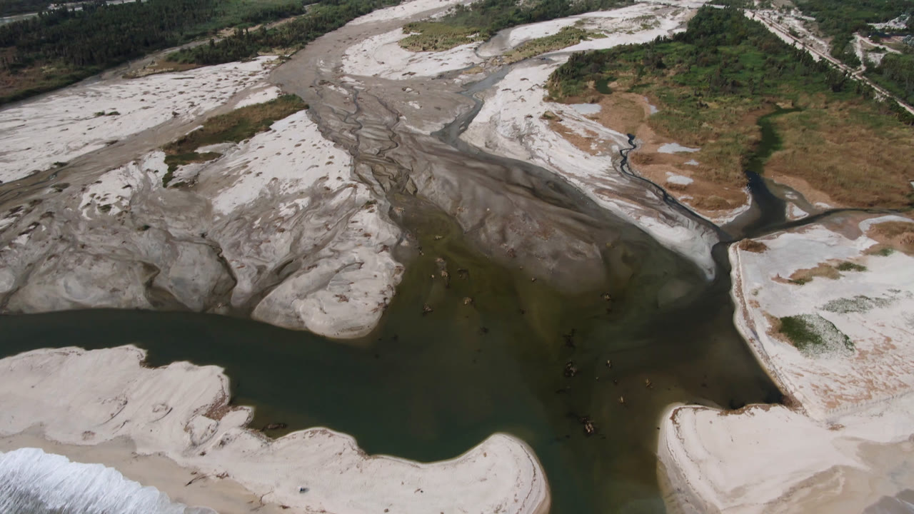 Wide aerial of a river confluence across pale sand and scrubland