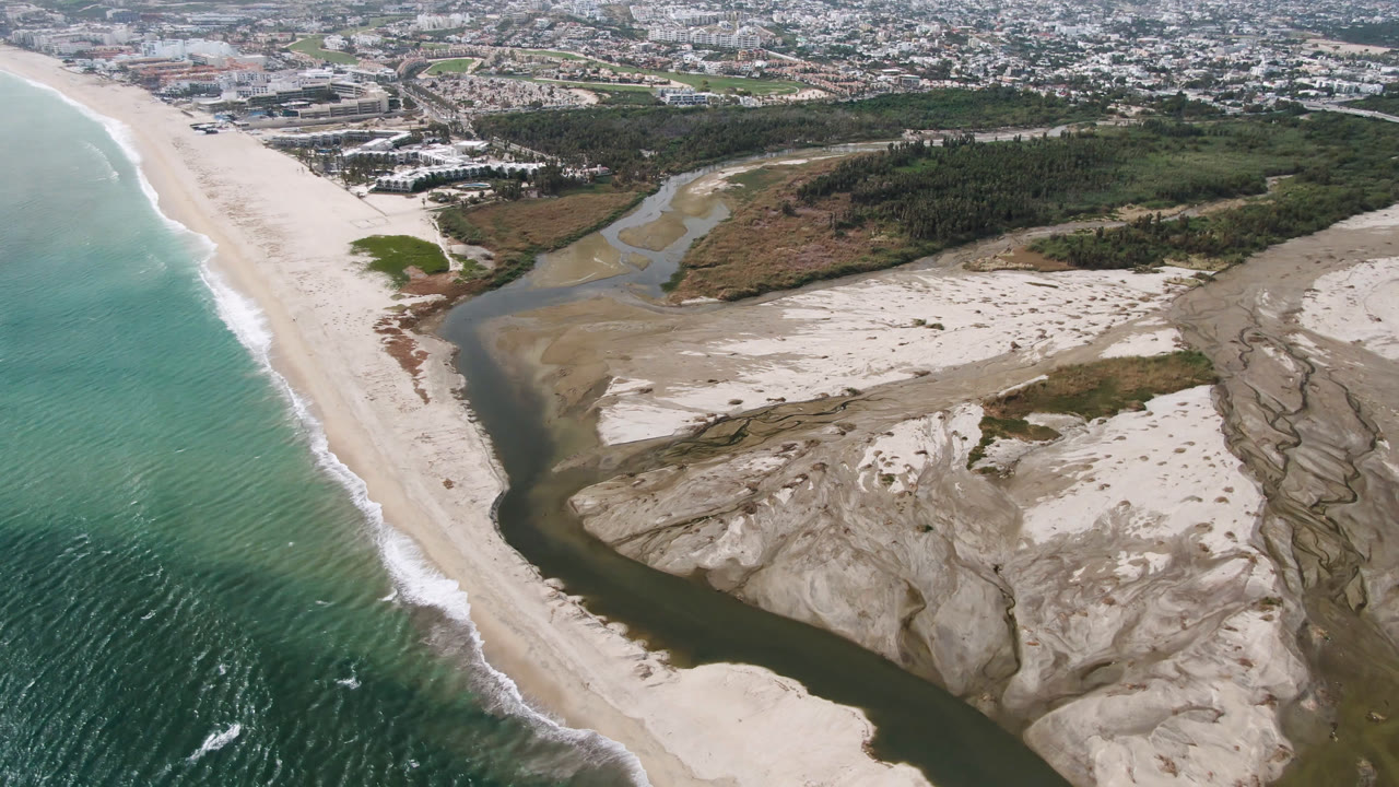 High aerial coastline with ocean, beach, river outlet, sand banks, shrubs, and town.