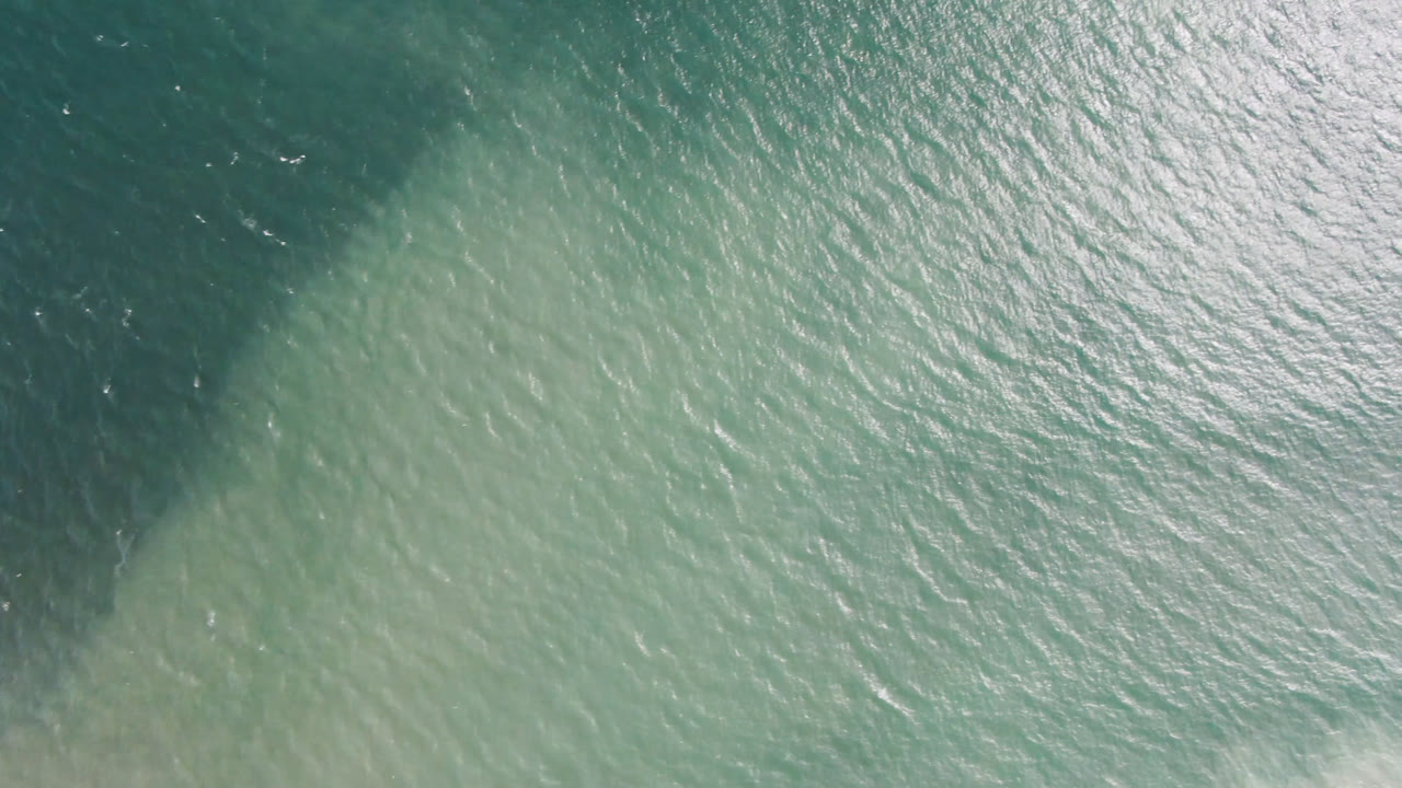 Top-down aerial view of teal ocean water in San Jose del Cabo with a dark underwater patch at the upper left and no visible people.