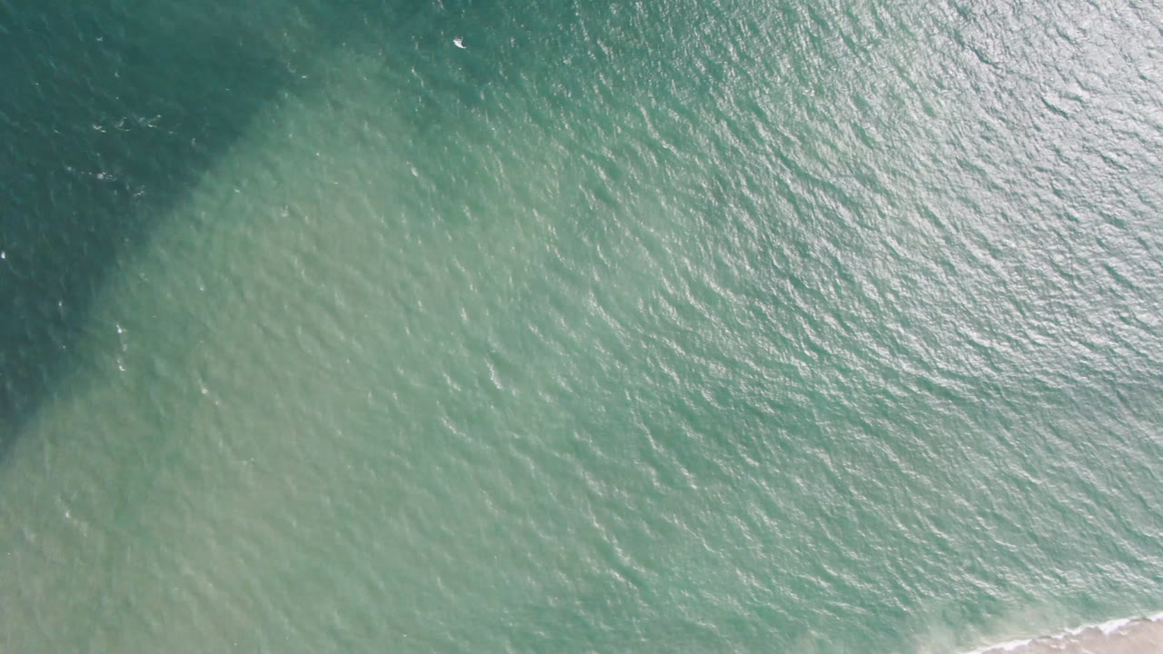 Sunlit ocean surface with dark water at the left and faint surf near the bottom.