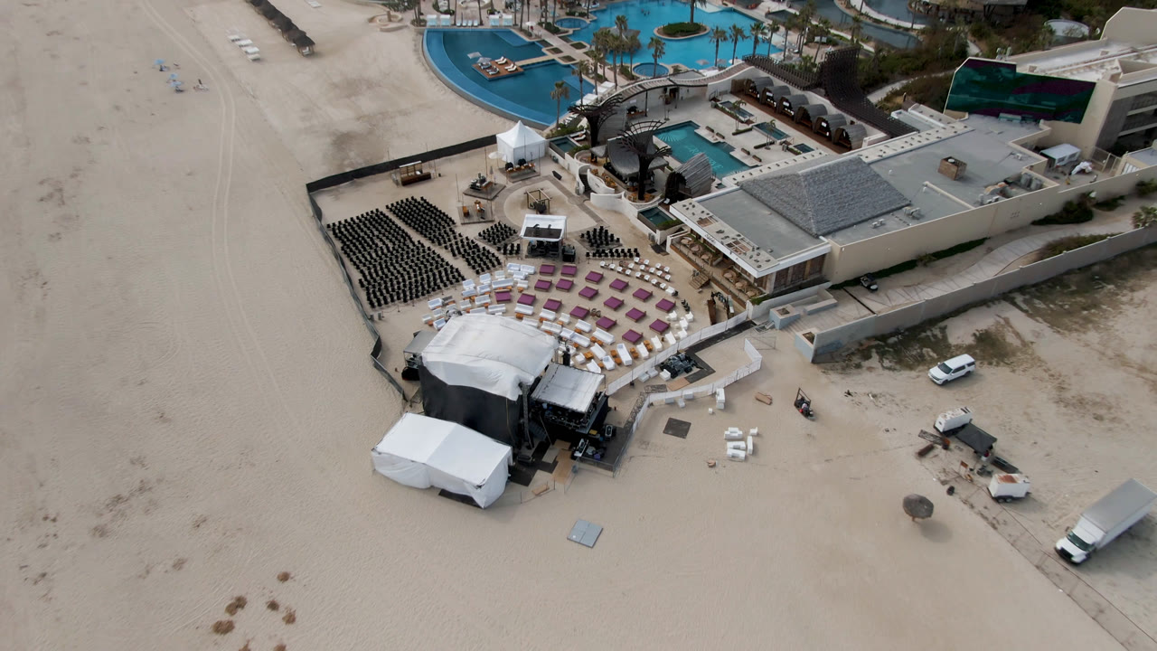 Drone view of resort pools and beach club seating near open sand.