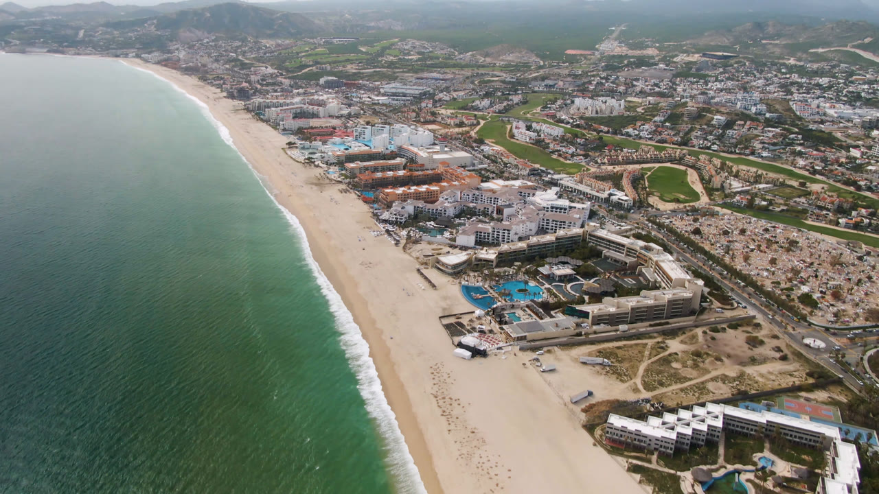 Drone view of beachfront resorts, ocean, beach, roads, city blocks, and mountains.