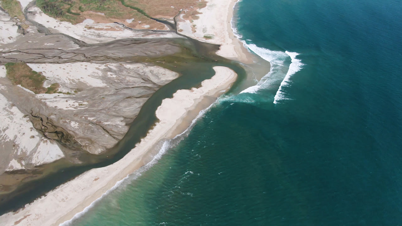 Overhead coastal frame in San Jose del Cabo with dark water wrapping around the sand banks, bright beach sand, offshore blue water, and no visible people.