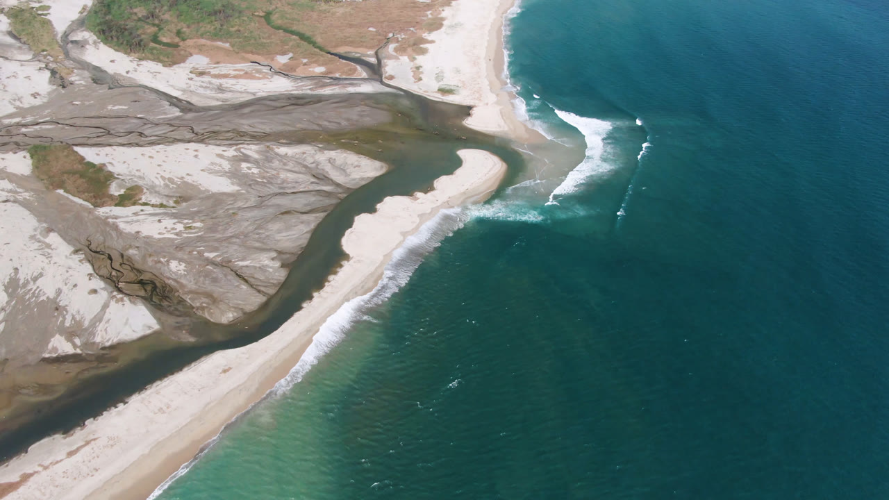 Aerial view in San Jose del Cabo with the curved sand spit centered, darker inlet water on the left, turquoise shallows below, and no visible people.