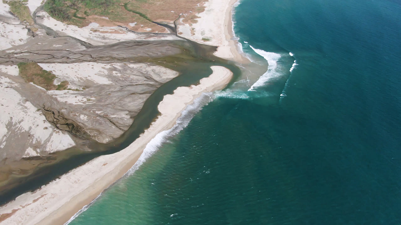 Overhead shoreline with sand bank, surf line, and open blue water.
