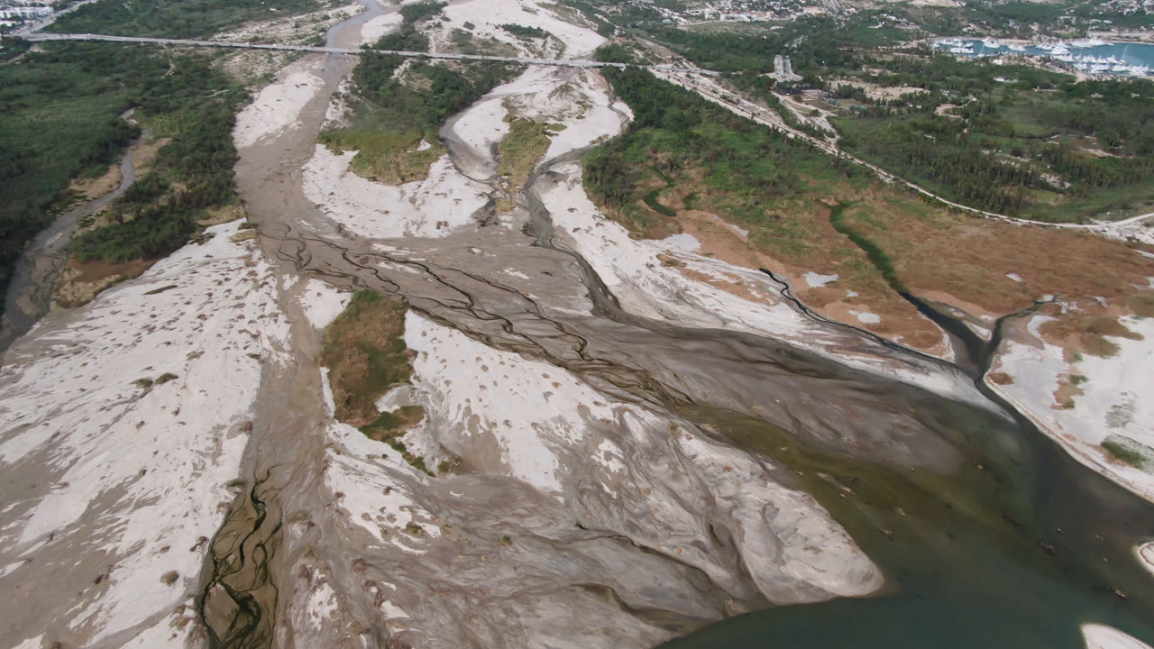 Aerial valley view with sandbars, a dark river bend, and development in the distance.
