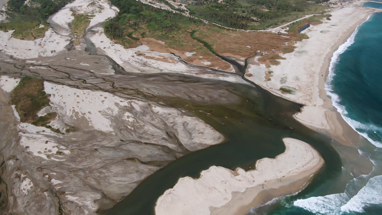 Aerial coastline with river mouth, pale beach, and breaking waves.