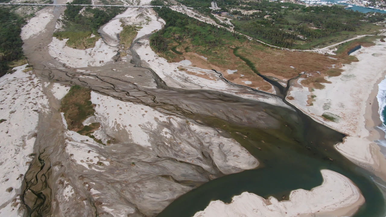 Aerial river mouth area with sand, scrubland, and distant ocean water.