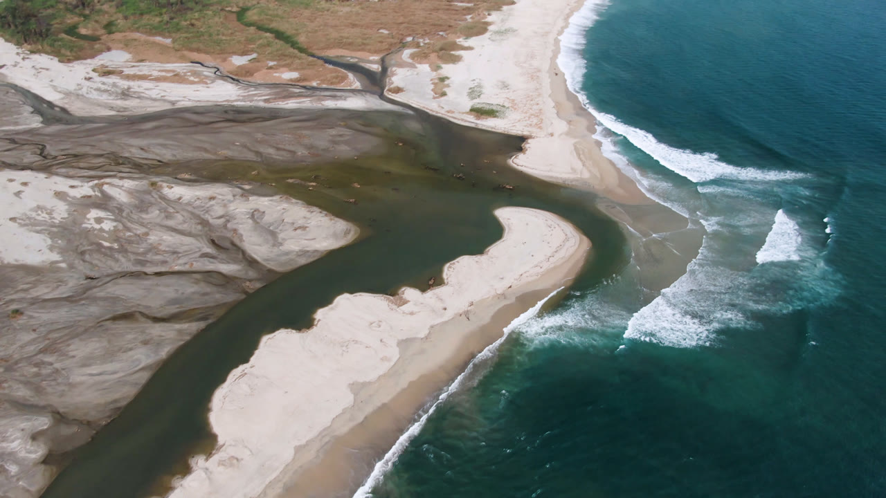 Curved sandbank between dark river water and ocean waves.