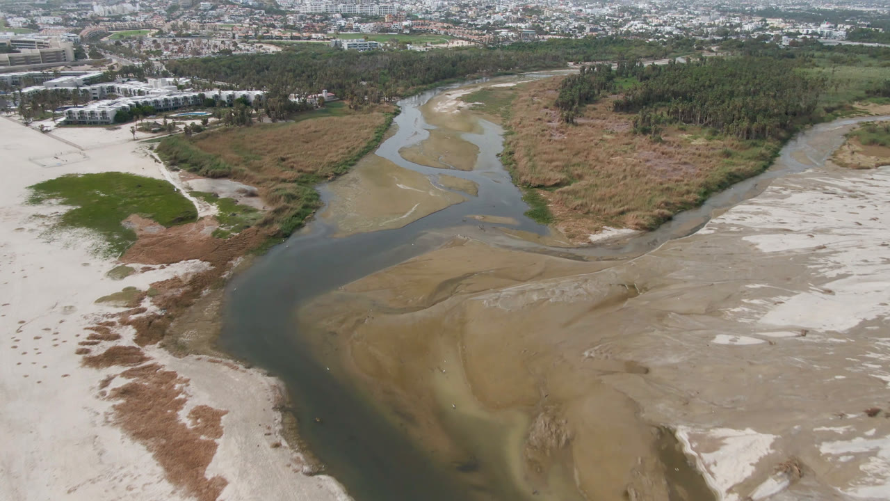 Aerial view of a sandy river mouth with vegetation and city beyond.