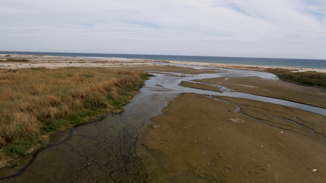 Sandy stream mouth and grassy edge with blue ocean in the distance.