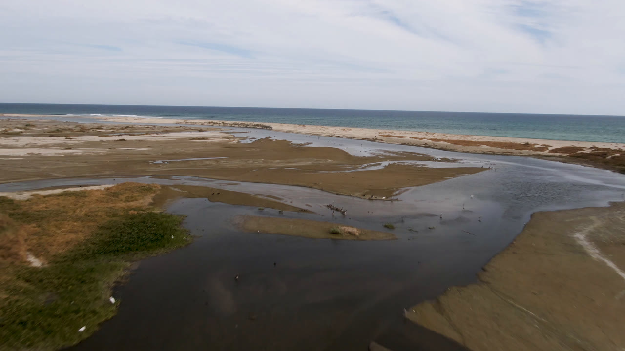 Aerial view in San Jose del Cabo, Baja California Sur, showing dark shallow water in the foreground, sand banks, a pale beach, ocean beyond, and no visible people.
