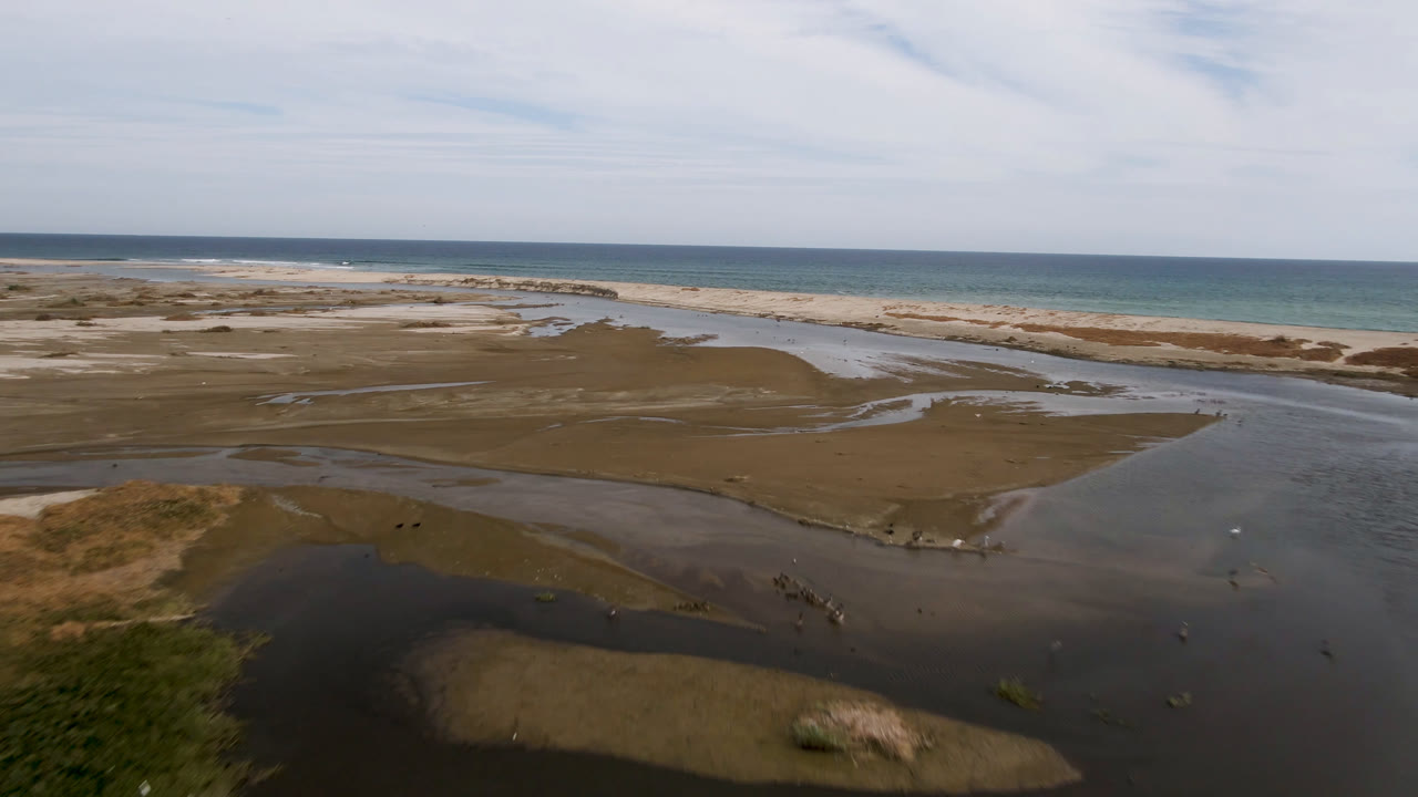 Aerial view over sand bars and shallow water leading to a beach and ocean.