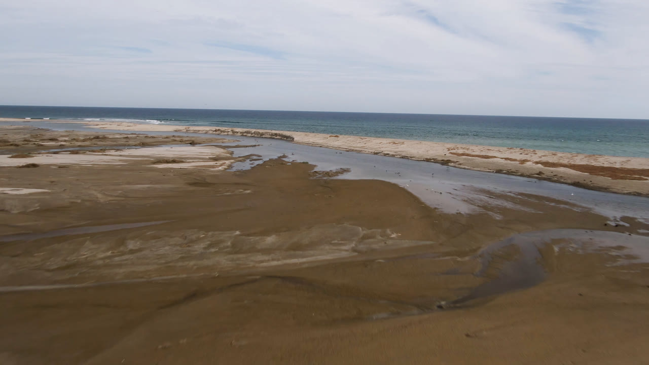 Aerial view of a shallow stream crossing sand banks toward the ocean.