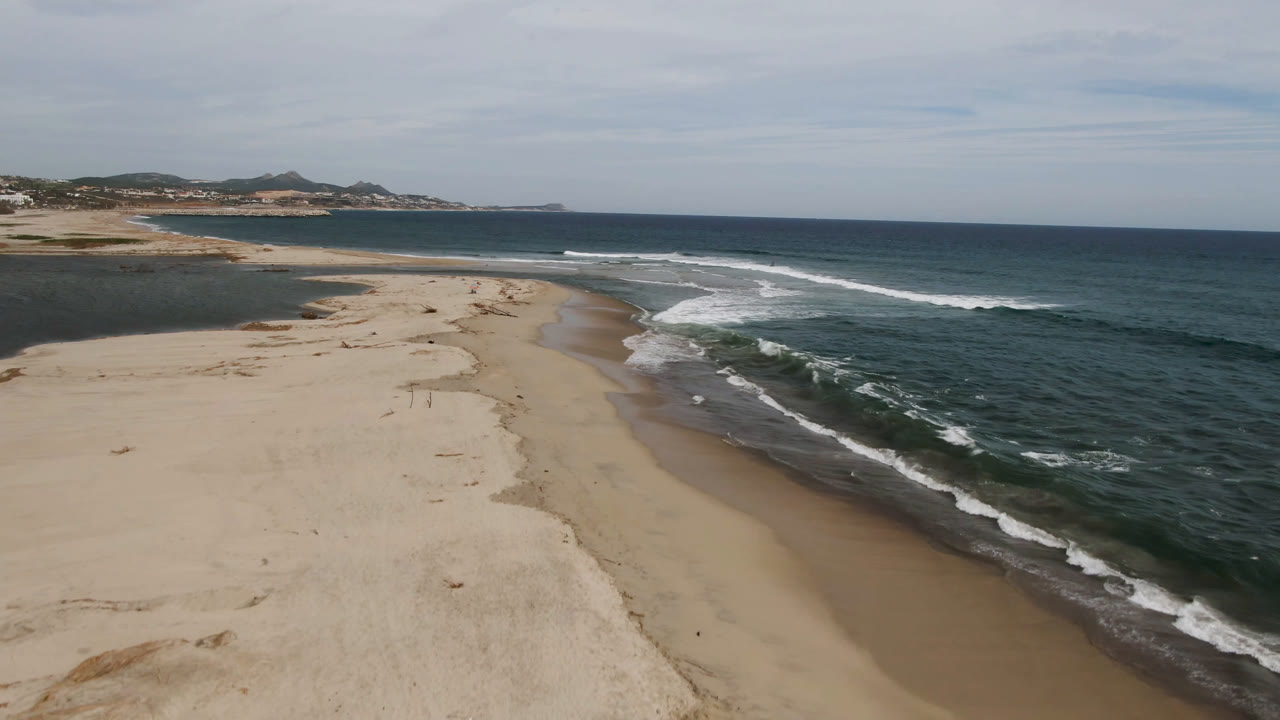 Elevated view of sandy beach and incoming waves under a cloudy sky.