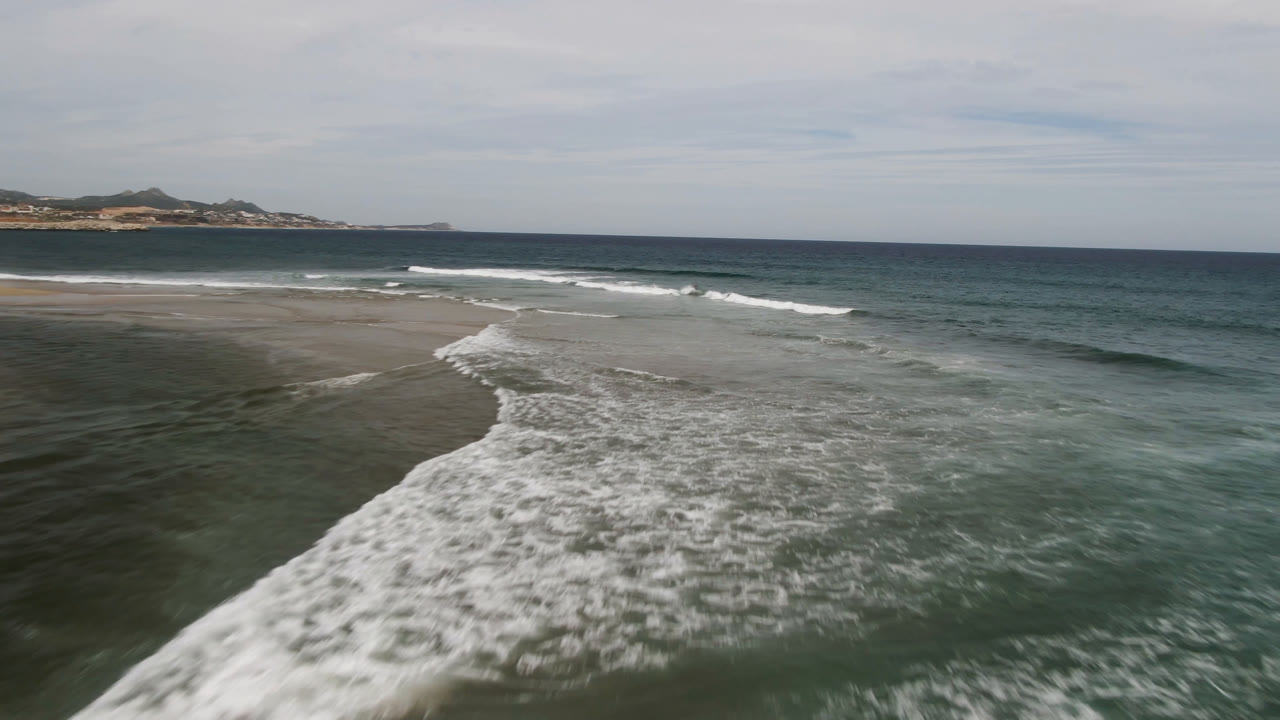 Aerial coastline view with a broad patch of white surf in the foreground.