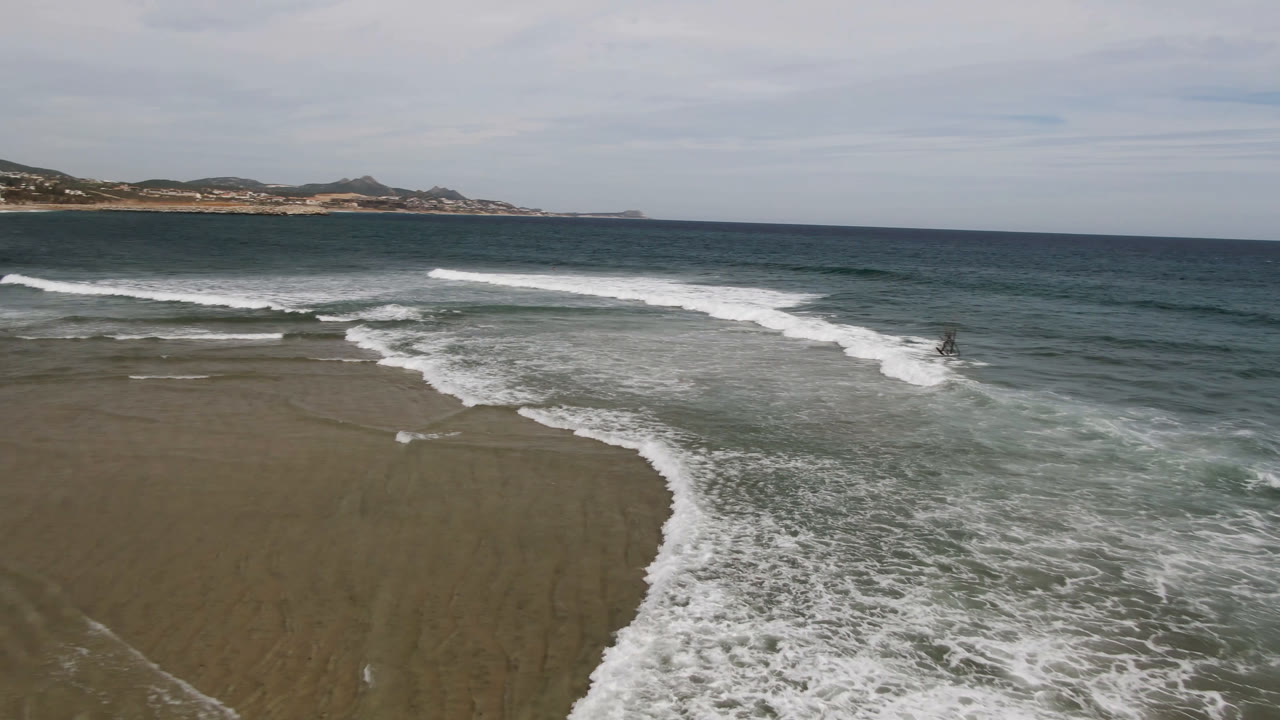 Aerial beach view with surf breaking diagonally toward wet sand.