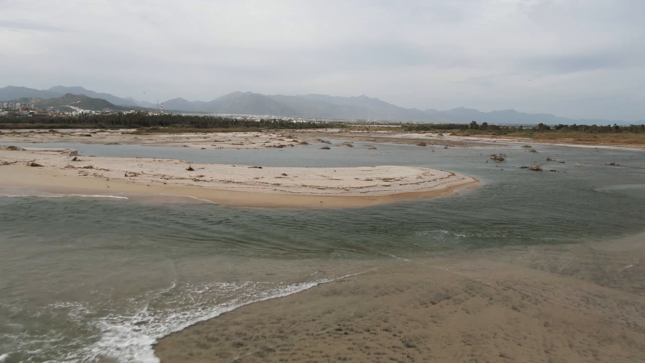 Aerial coastal landscape with foreground waves, central sand, and mountain backdrop