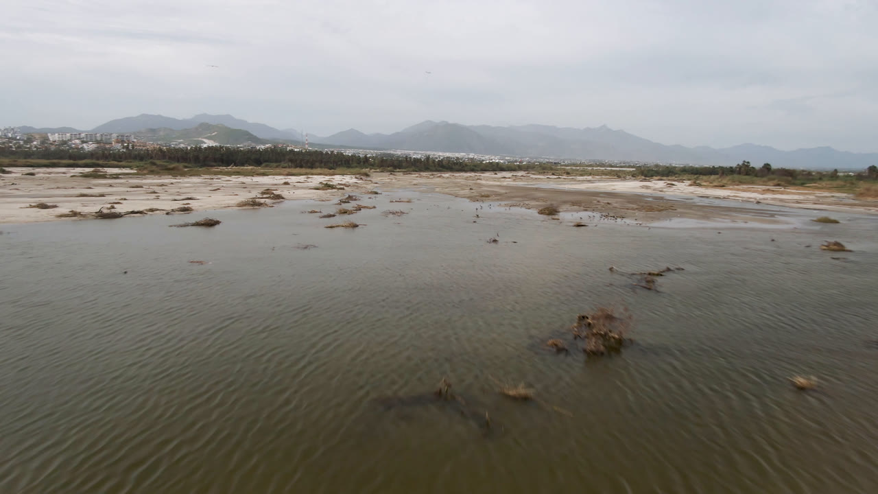 Rippling water foreground with a larger rock clump and mountains beyond the shore.