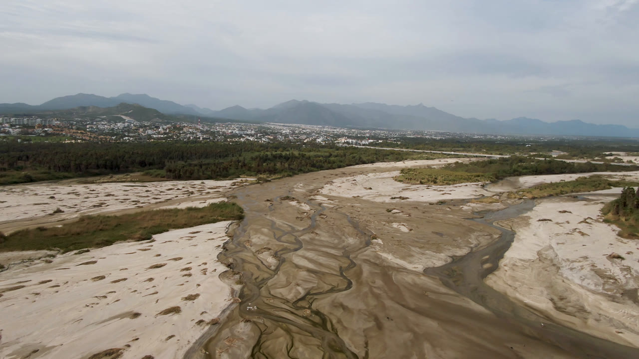 Aerial view of a sandy riverbed with a narrow stream and distant mountains.