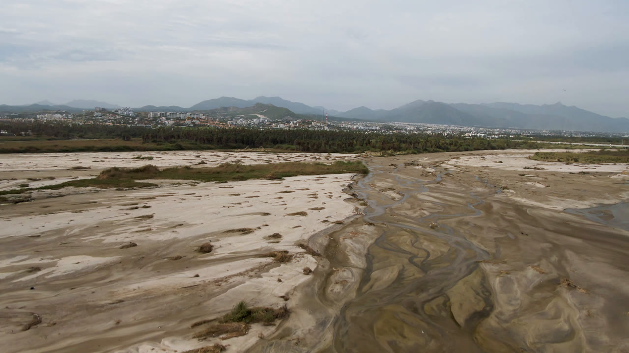 Aerial view of a sandy riverbed with narrow water channels and distant mountains.