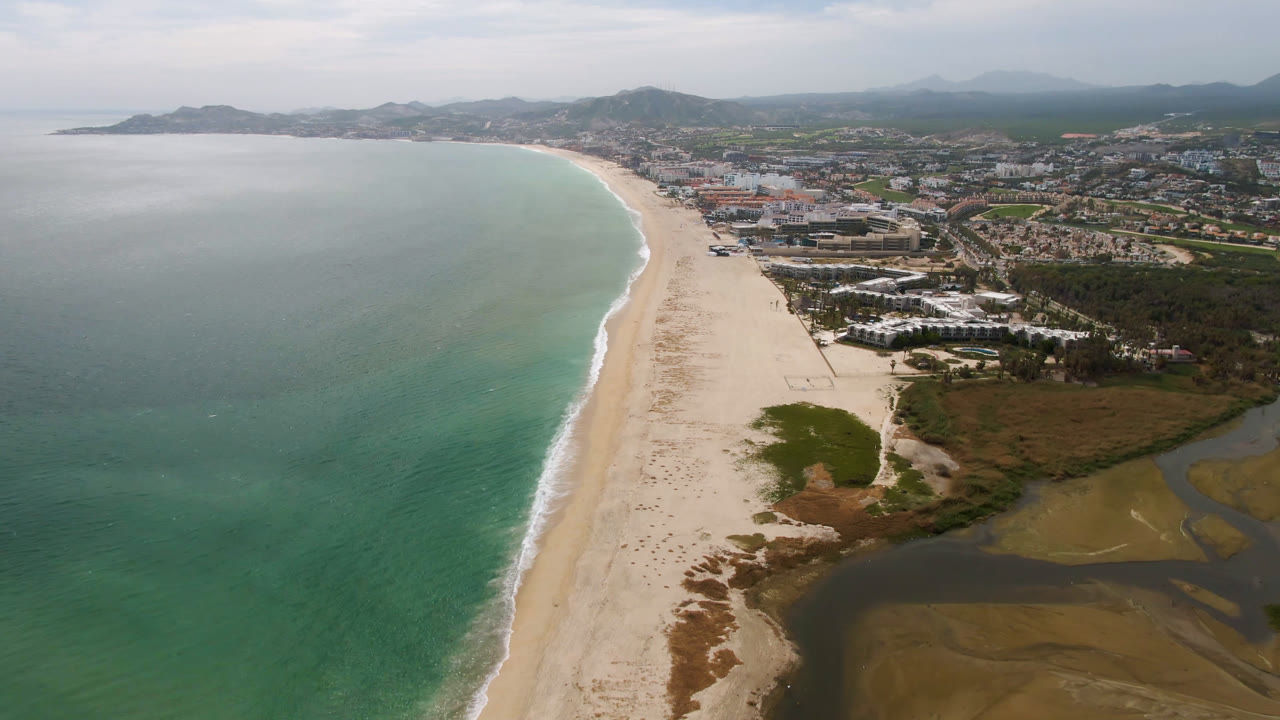 Wide aerial coastline with beach, ocean, city blocks, and mountains