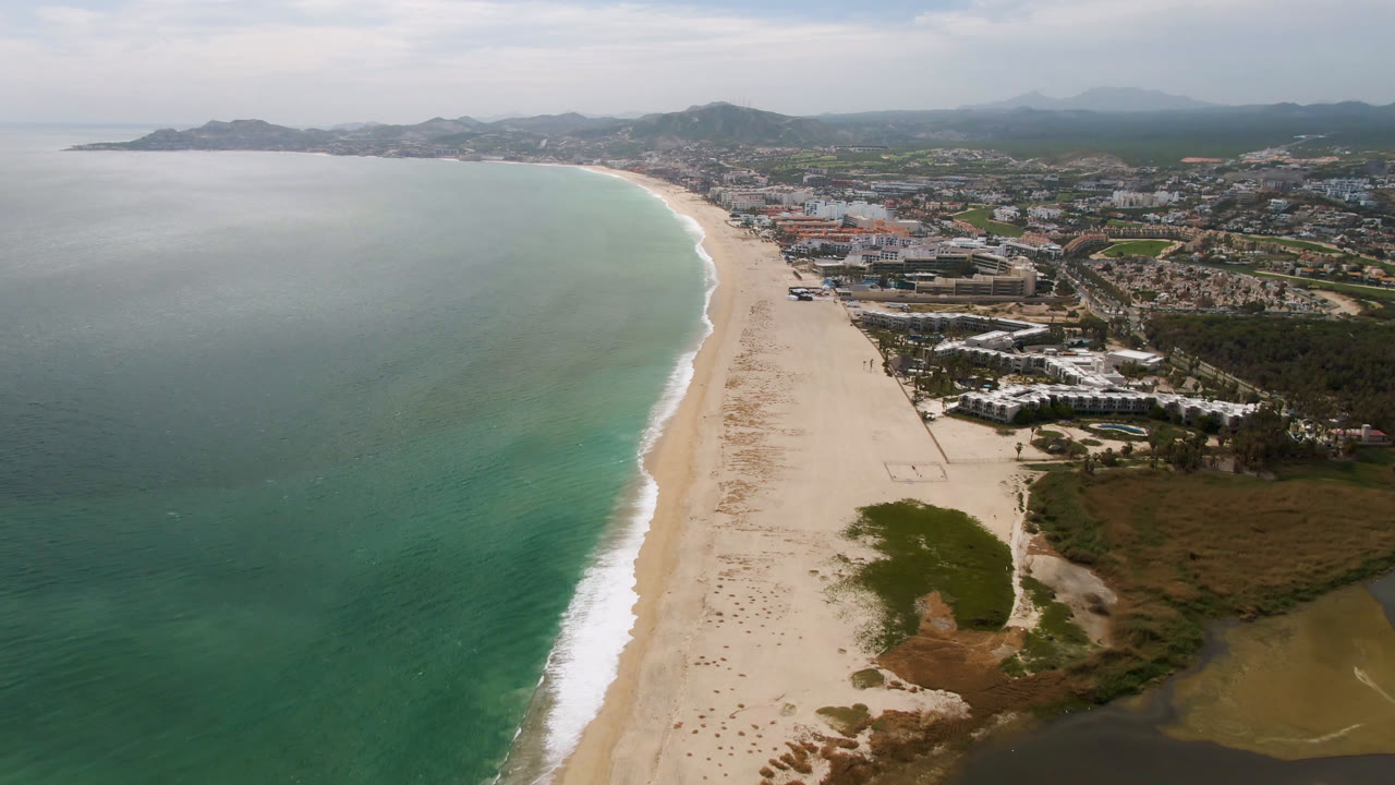 Wide aerial beach scene with ocean at left and city inland.