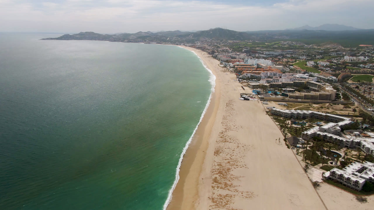 Aerial view of ocean, beach, beachfront buildings, and distant hills