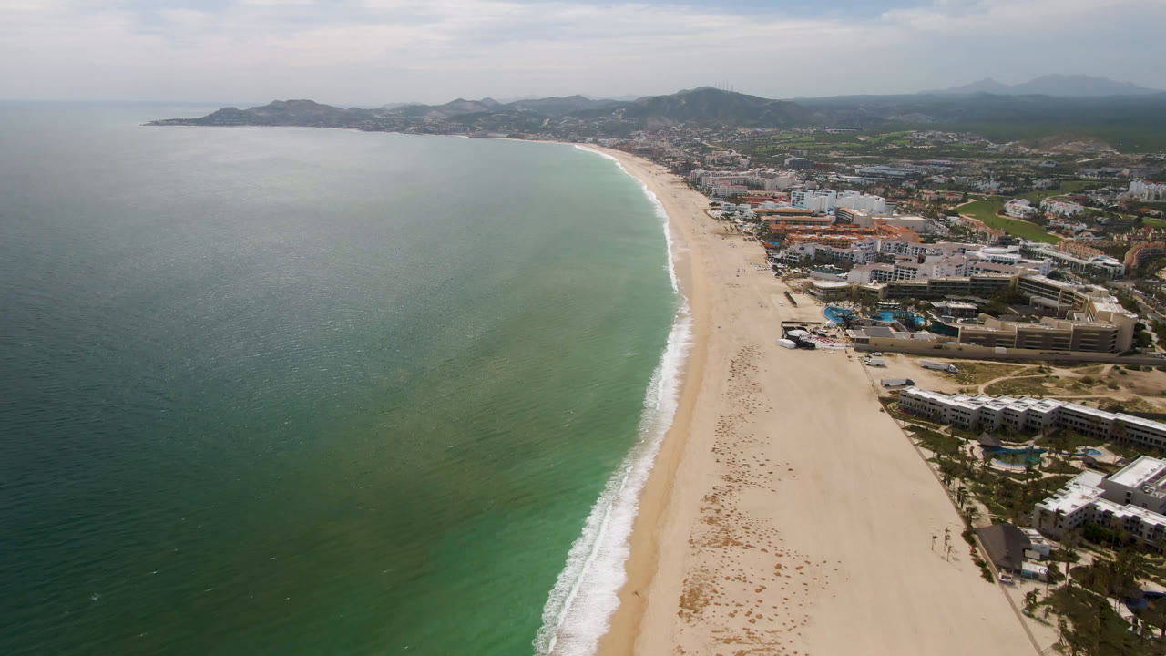 Drone view of beach and ocean with buildings along the right side.