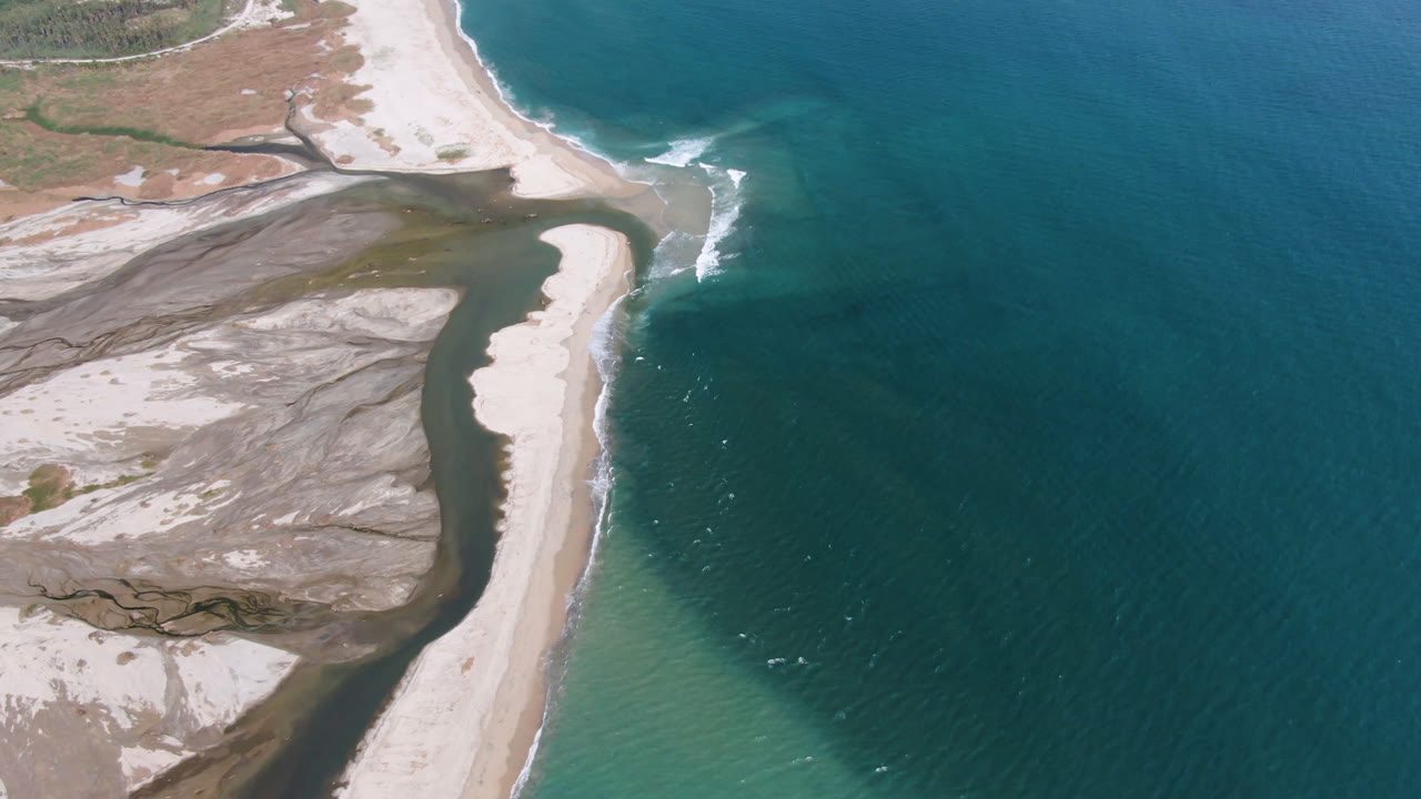 Aerial frame over San Jose del Cabo showing pale sand banks curving along dark water, white surf at the shore, and no visible people.