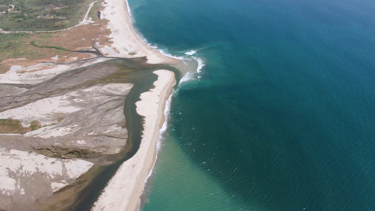 Drone view of beach, inlet, and offshore blue water with small surf lines.