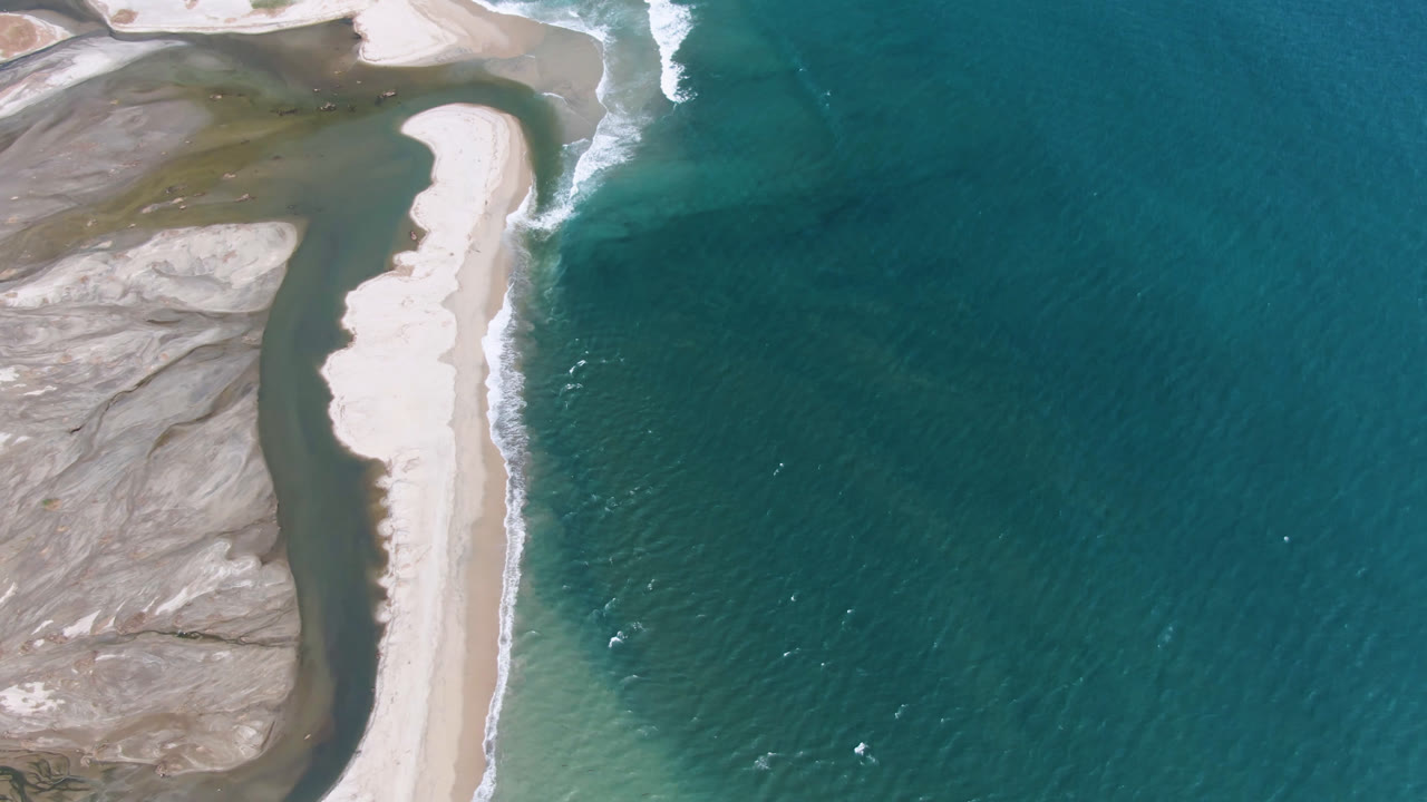 Aerial shoreline with pale sand, darker ocean water, and exposed flats.