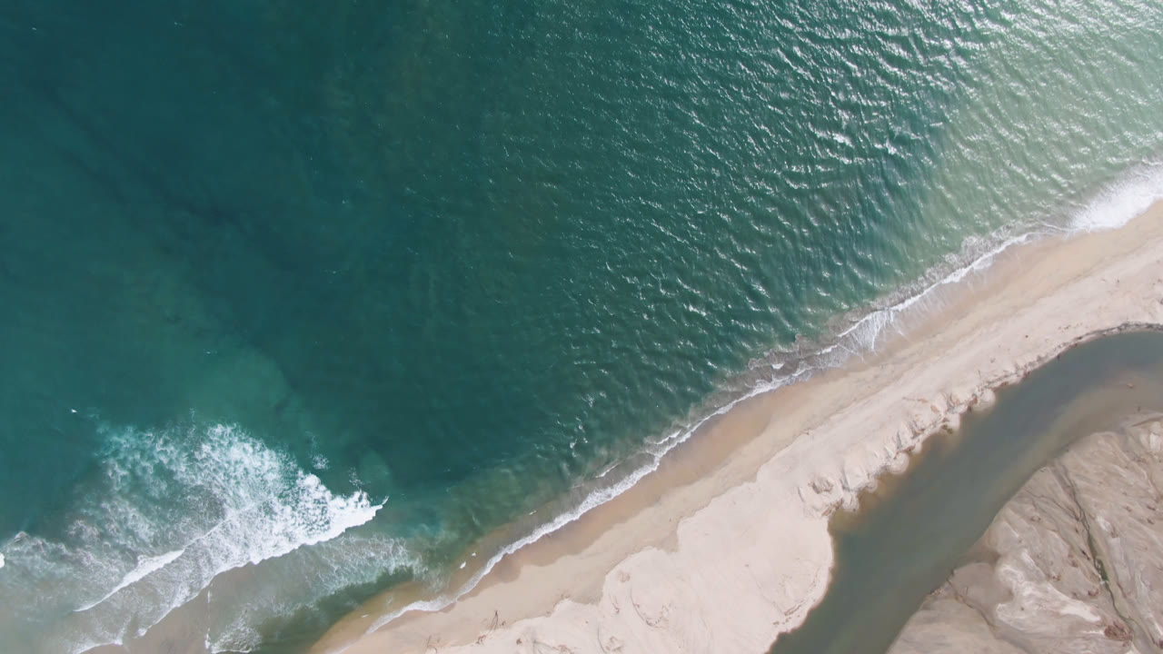 Top-down beach edge with wave foam sliding along shore