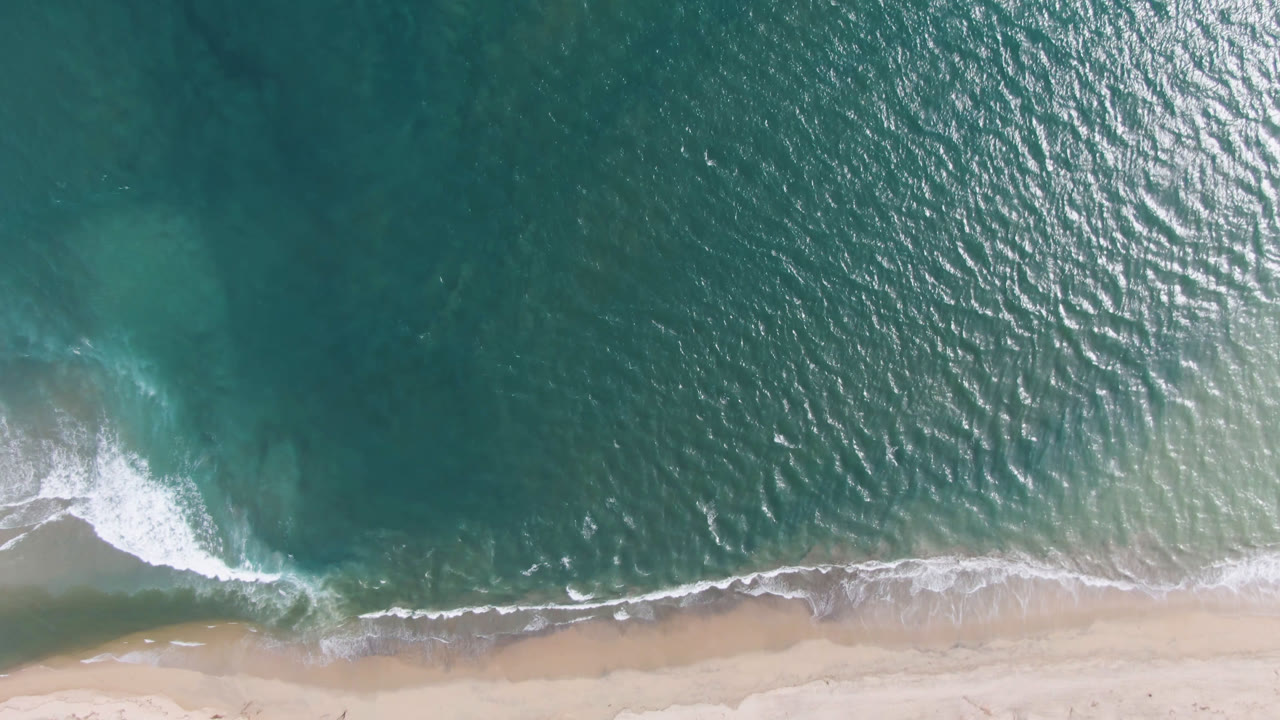 Top-down ocean edge with bright ripples and beach foam.