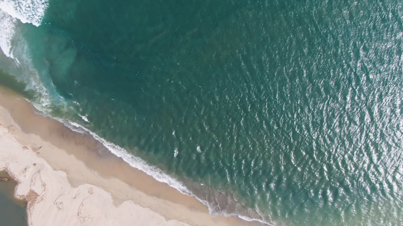 Top-down beach and ocean with surf breaking near the sand