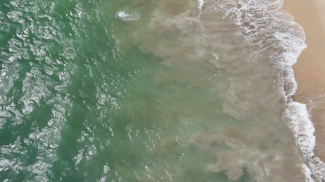 Top-down surf line with pale sand and textured green water.