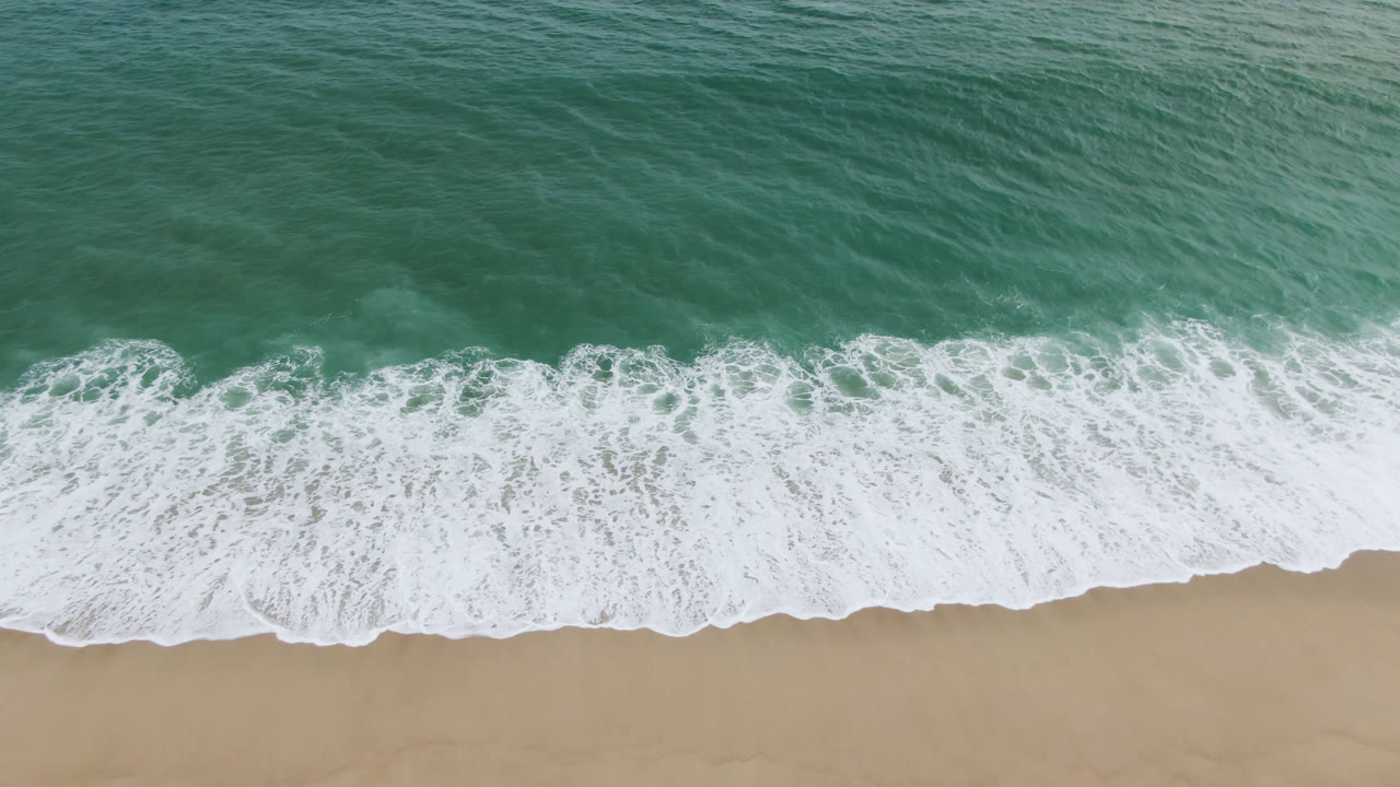 Surfboard near foamy shoreline from above